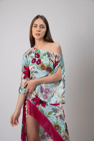 Close-up front view of model wearing a blue floral beach dress with off-shoulder slit sleeves and fringe-detailed hem.