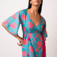 Front-facing pose of model in floral blue muslin dress with side tie-up and flared hem, holding one hand at the waist.
