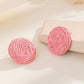 A pair of vibrant statement earrings featuring a small pink raffia stud and a larger, hollow circular drop woven from bright pink raffia