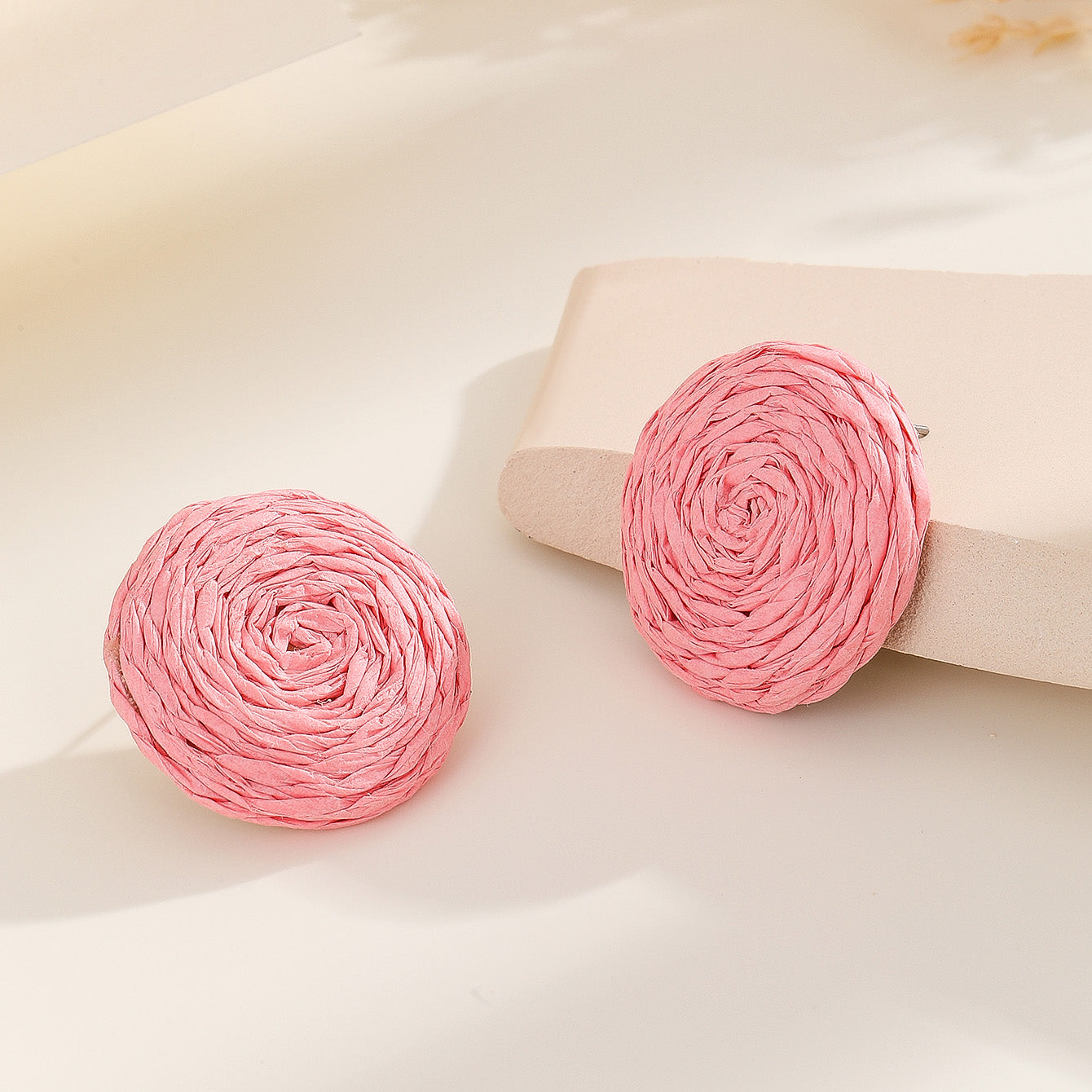 A pair of vibrant statement earrings featuring a small pink raffia stud and a larger, hollow circular drop woven from bright pink raffia