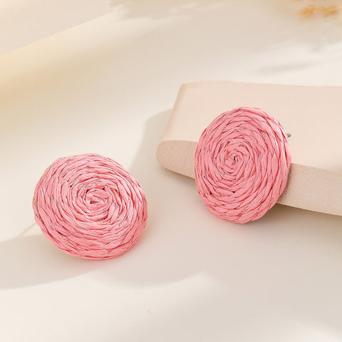 A pair of vibrant statement earrings featuring a small pink raffia stud and a larger, hollow circular drop woven from bright pink raffia