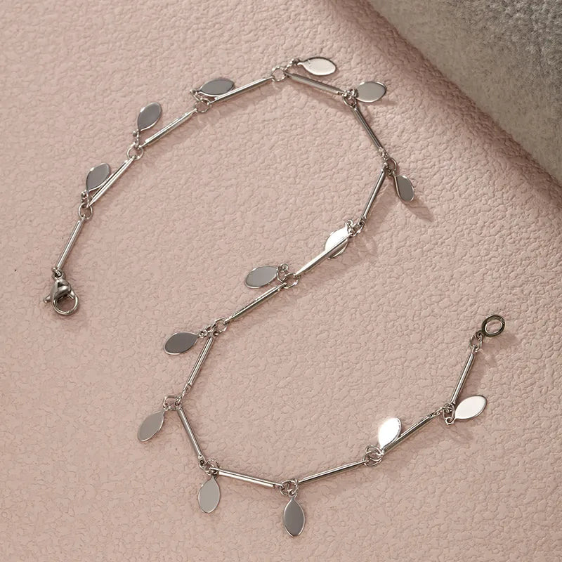 A refined sterling silver anklet featuring a series of polished, flat oval charms that catch the light, perfect for adding a sophisticated sparkle to  a cocktail party.