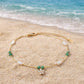 A delicate and feminine gold-toned anklet with a sparkling flower centerpiece and olive green accents, designed to add a graceful touch to your summer vacation.