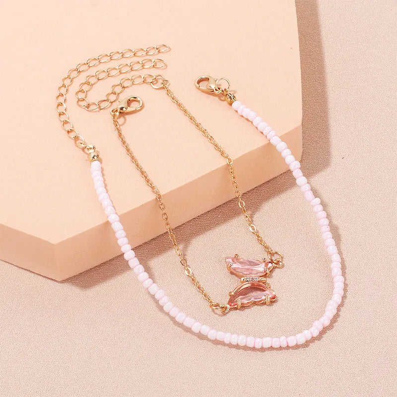 A vibrant pink seed bead anklet featuring a delicate, translucent pink butterfly charm that catches the light