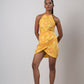 Full-frontal zoomed out view of model standing confidently in yellow halter dress, arms relaxed by her side.